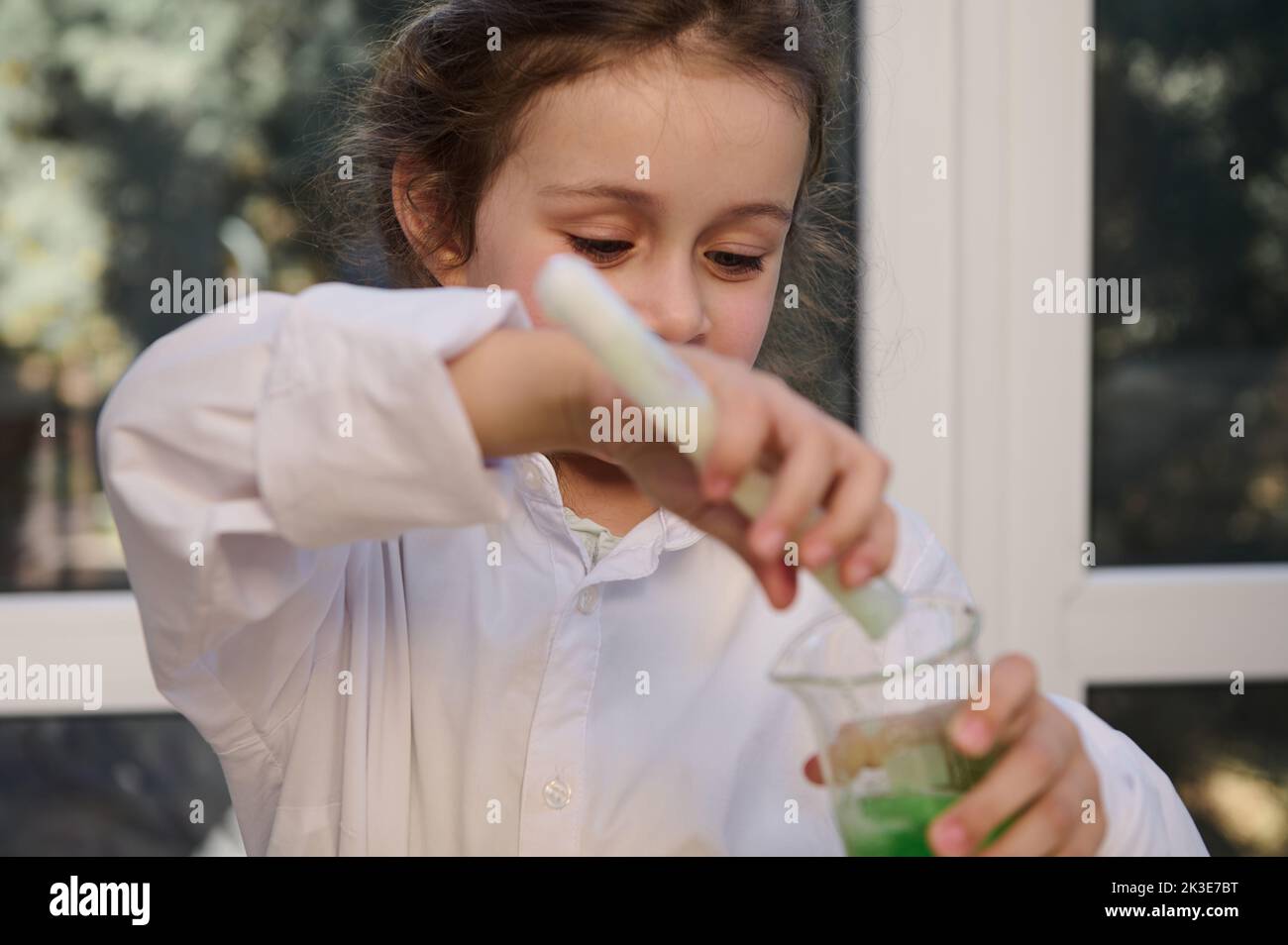 Mischievous preschool girl conducts chemical experiment, pours liquid