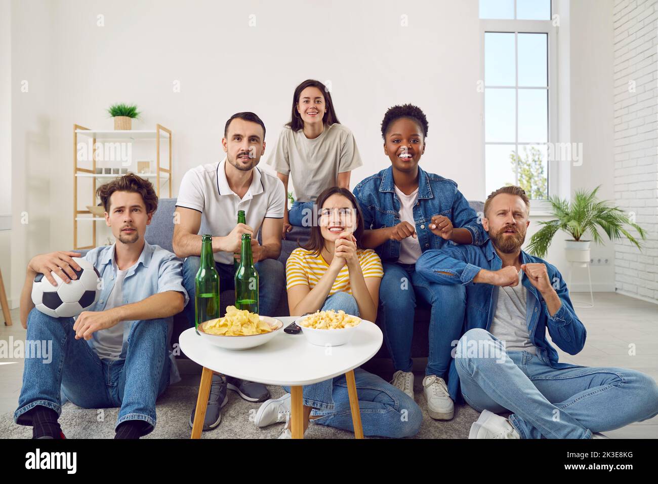 Group of happy diverse friends watching football on TV while sitting on sofa at home Stock Photo