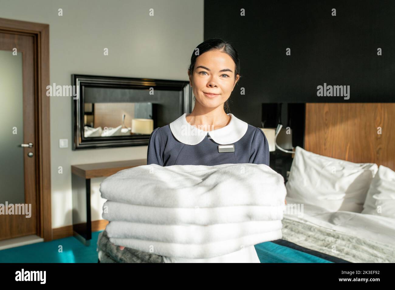 Photo realistic digital collage of happy room service staff holding stack of white clean sheets in bedroom Stock Photo