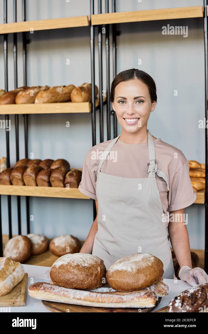 Ai generated face of happy young female baker standing by workplace and selling fresh bread Stock Photo