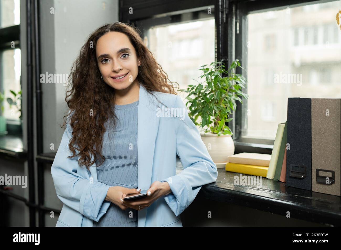 Ai generated face of happy young businesswoman with dark long wavy hair standing by window Stock Photo