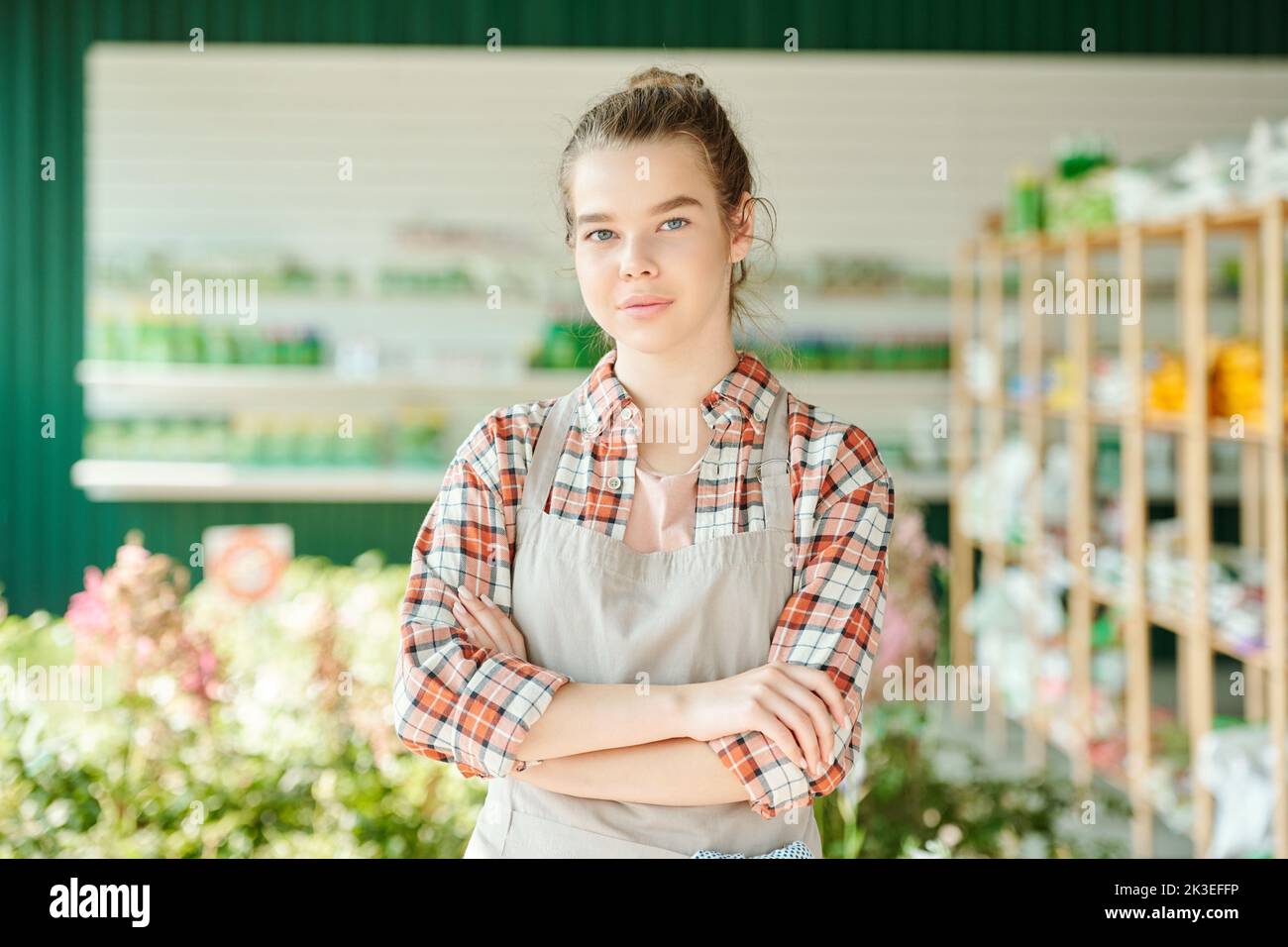 Ai generated face of young pretty female farmer or shop assistant with crossed arms standing in front of camera against supermarket interior Stock Photo