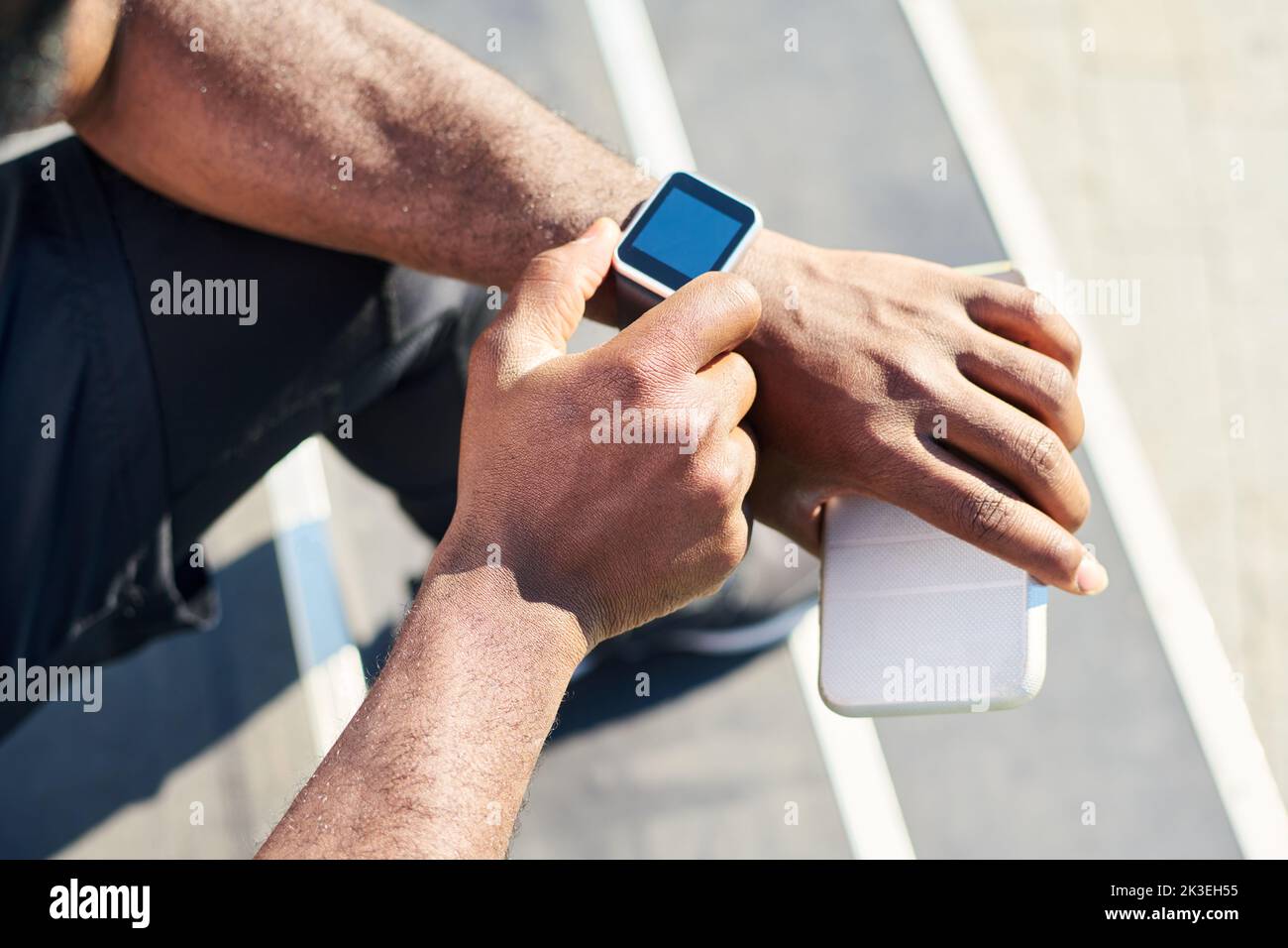 Hands of young black man sitting on staircase and checking or noting time on wristwatch before outdoor sports training or jogging Stock Photo