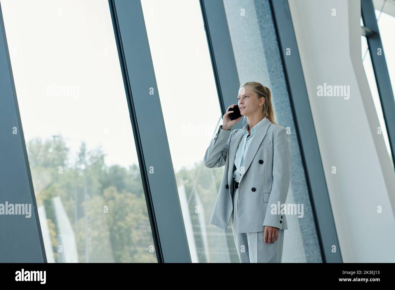 Young blond female agent or manager in formalwear talking on smartphone while arranging appointment with client Stock Photo