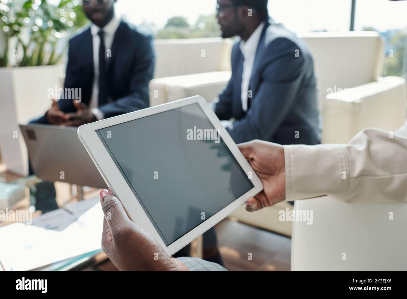 Tablet with black screen in hands of young African American businesswoman networking against two male coworkers Stock Photo