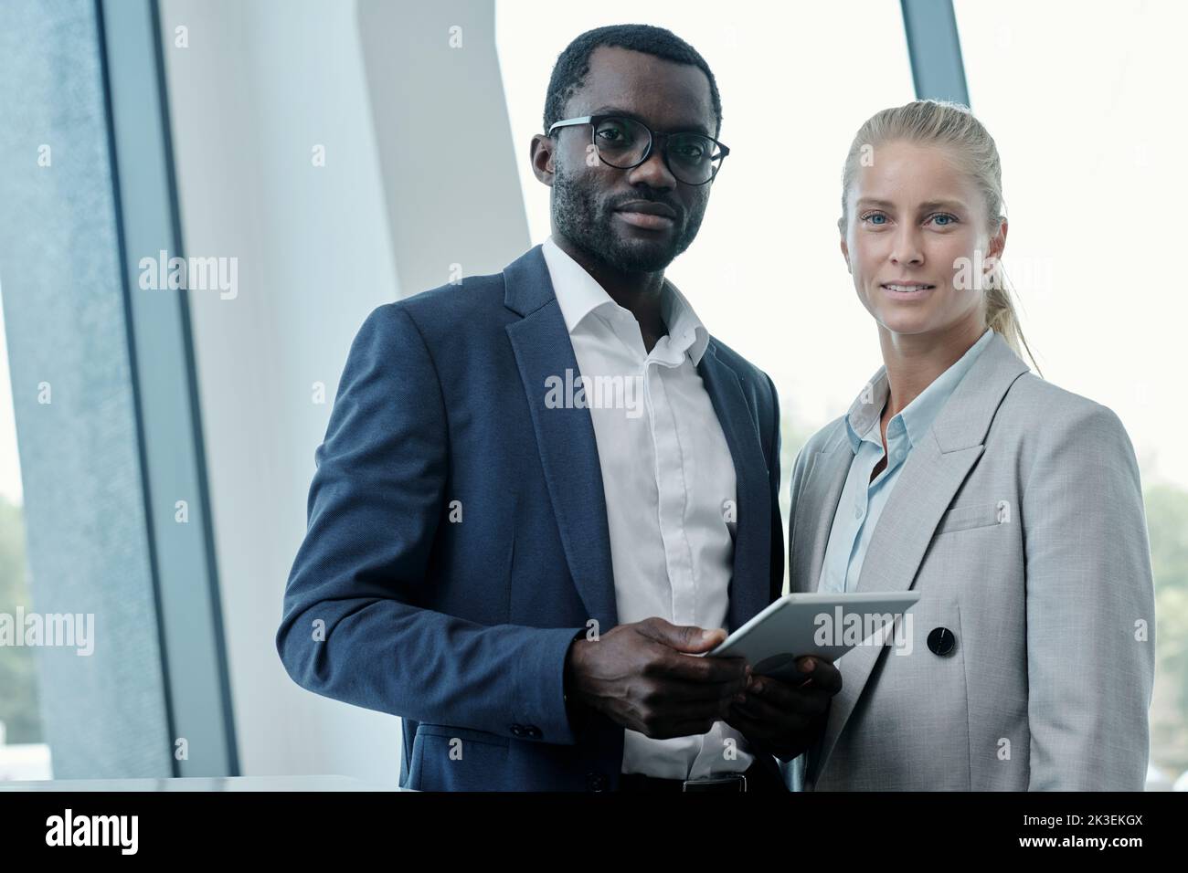 Portrait of two young intercultural office managers or business partners in elegant suits looking at camera while preparing presentation Stock Photo