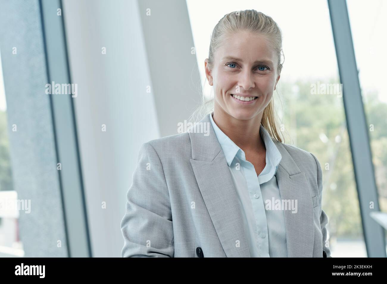 Young successful manager of business company in formalwear looking at camera with toothy smile while standing against office window Stock Photo