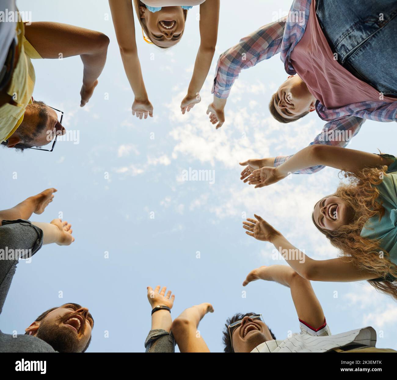 Diverse team of happy excited young friends raising their hands up in the blue sky Stock Photo