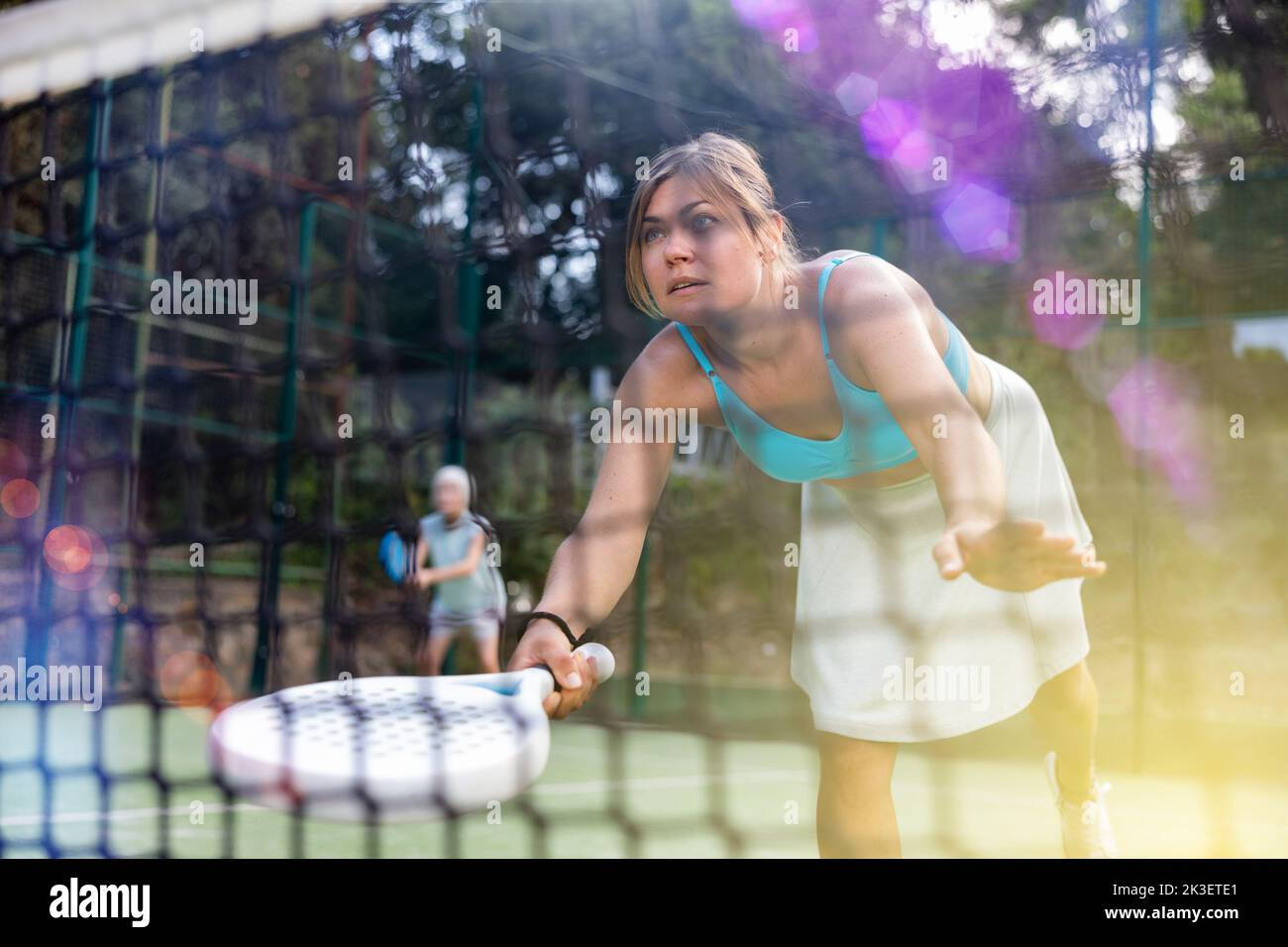View through net of young female paddle tennis player hitting ball Stock Photo