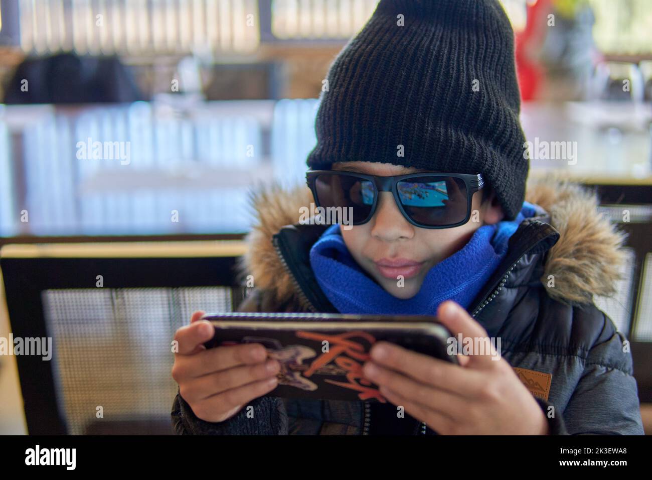 latino kid with sunglasses and a wool cap using the cell phone very cool. Wintertime. Focus on foreground Stock Photo