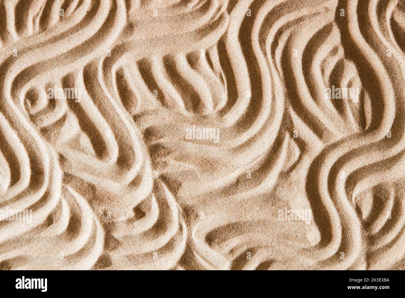 Natural beige sand texture background with wave pattern. Wavy curved ornaments on sand, drawn by hand. Top view Stock Photo