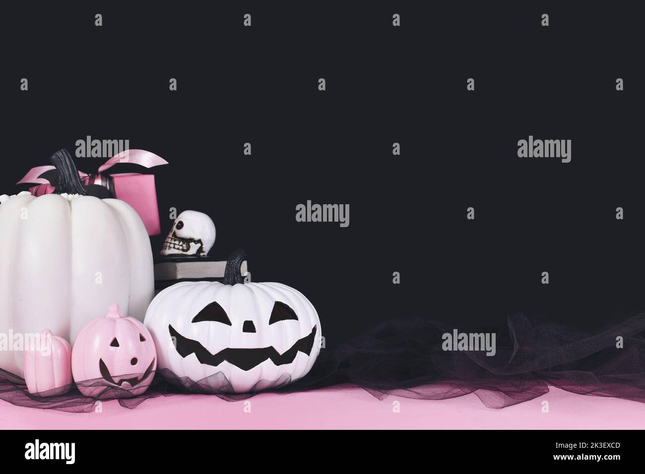 Pink and white Halloween decor with black and white pumpkins, spell books and spiders on black background  with copy space Stock Photo