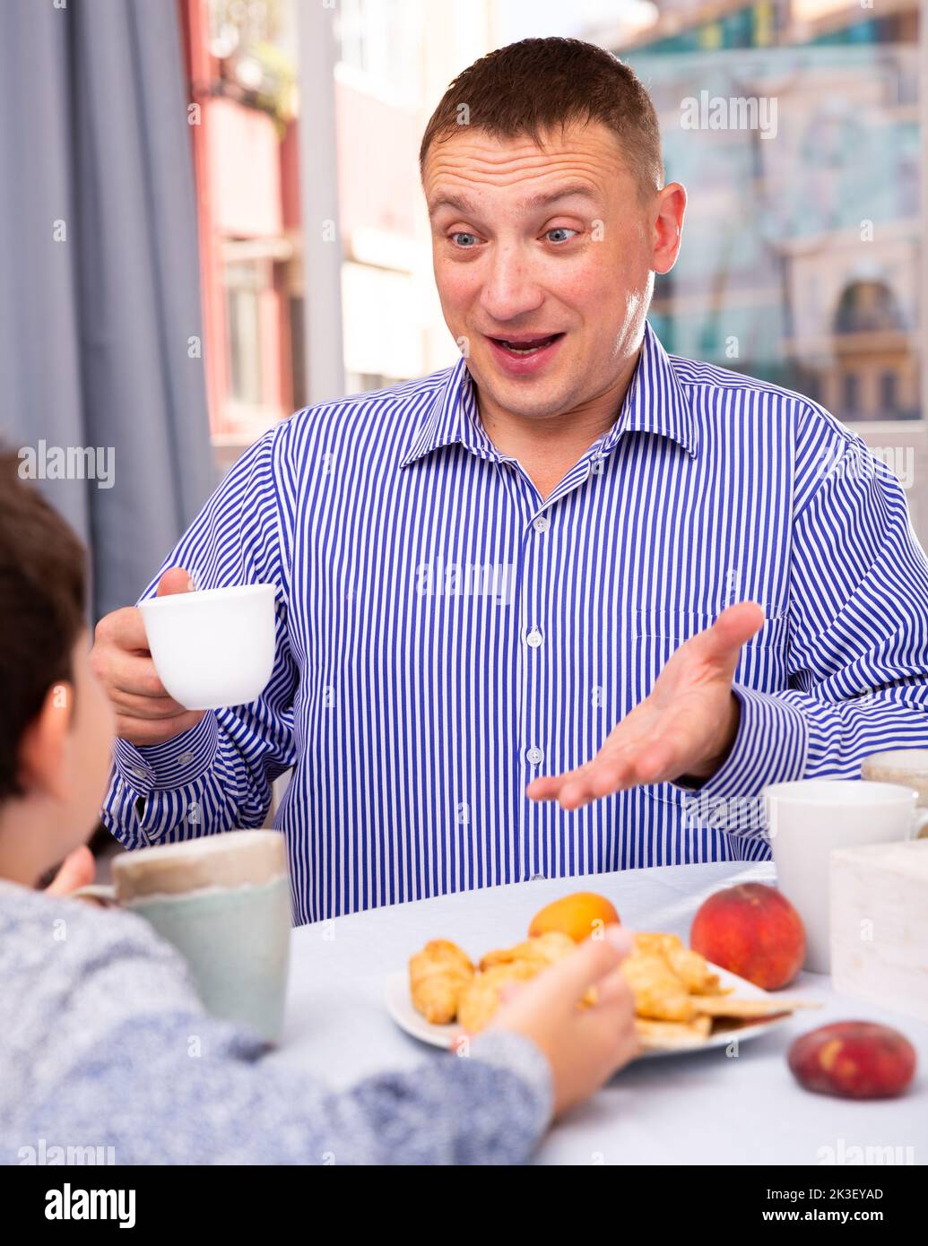 Young man chatting with his son at table with tea during breakfast Stock Photo