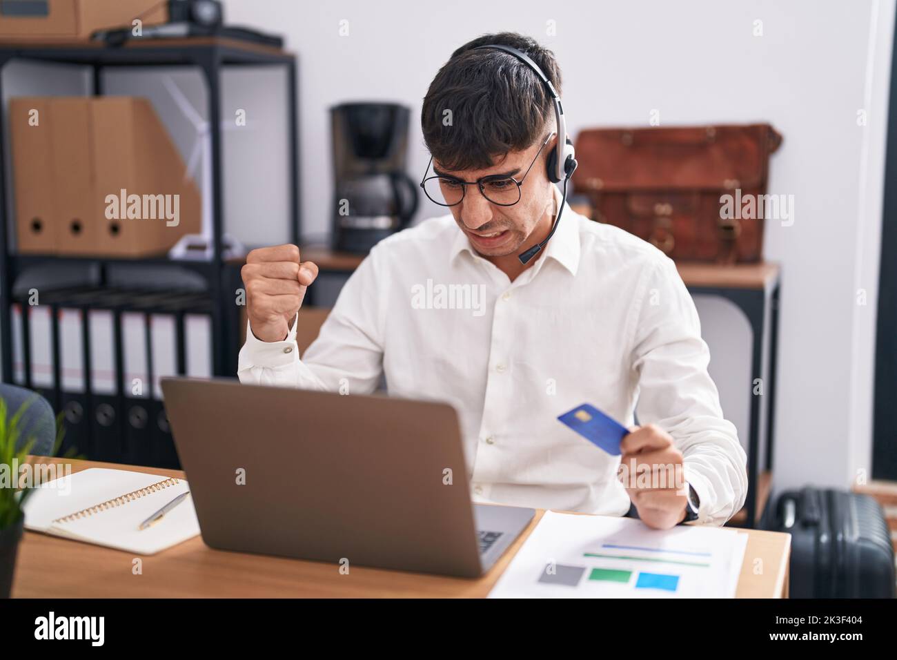 Young hispanic man working using computer laptop holding credit card ...