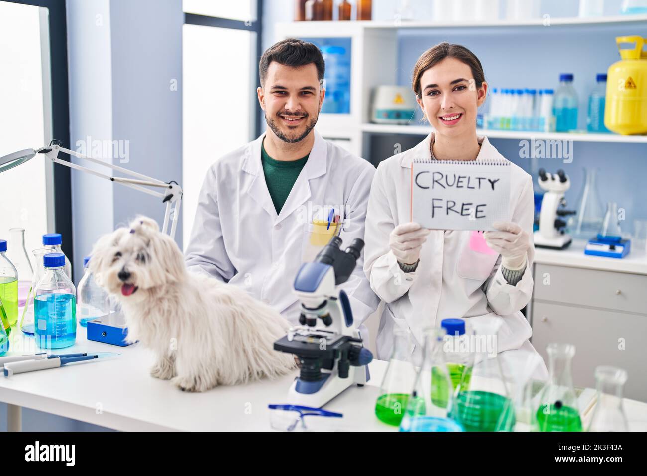 Young hispanic people working at scientist laboratory with dog smiling with a happy and cool smile on face. showing teeth. Stock Photo