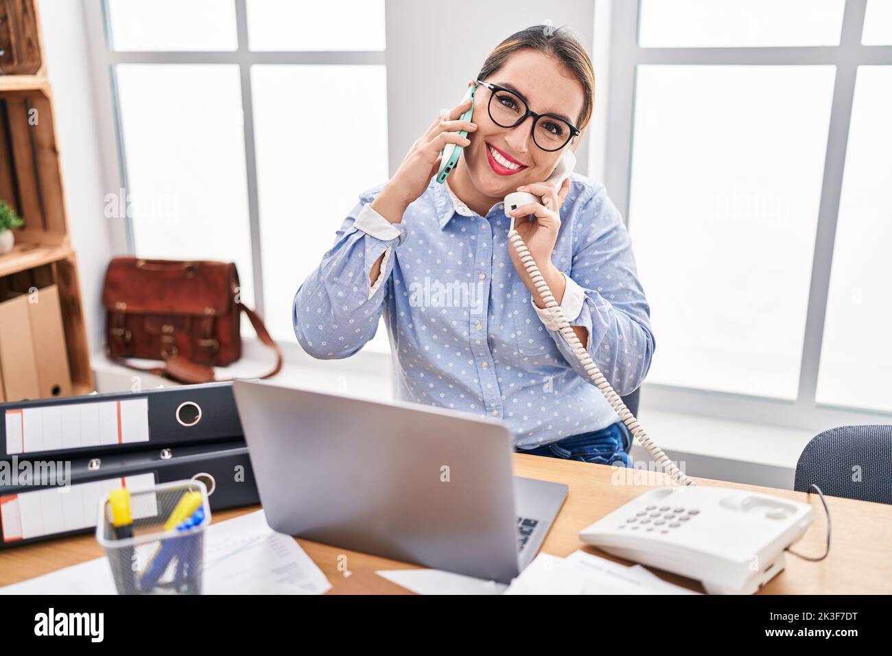 Young hispanic business woman working at the office talking on two ...