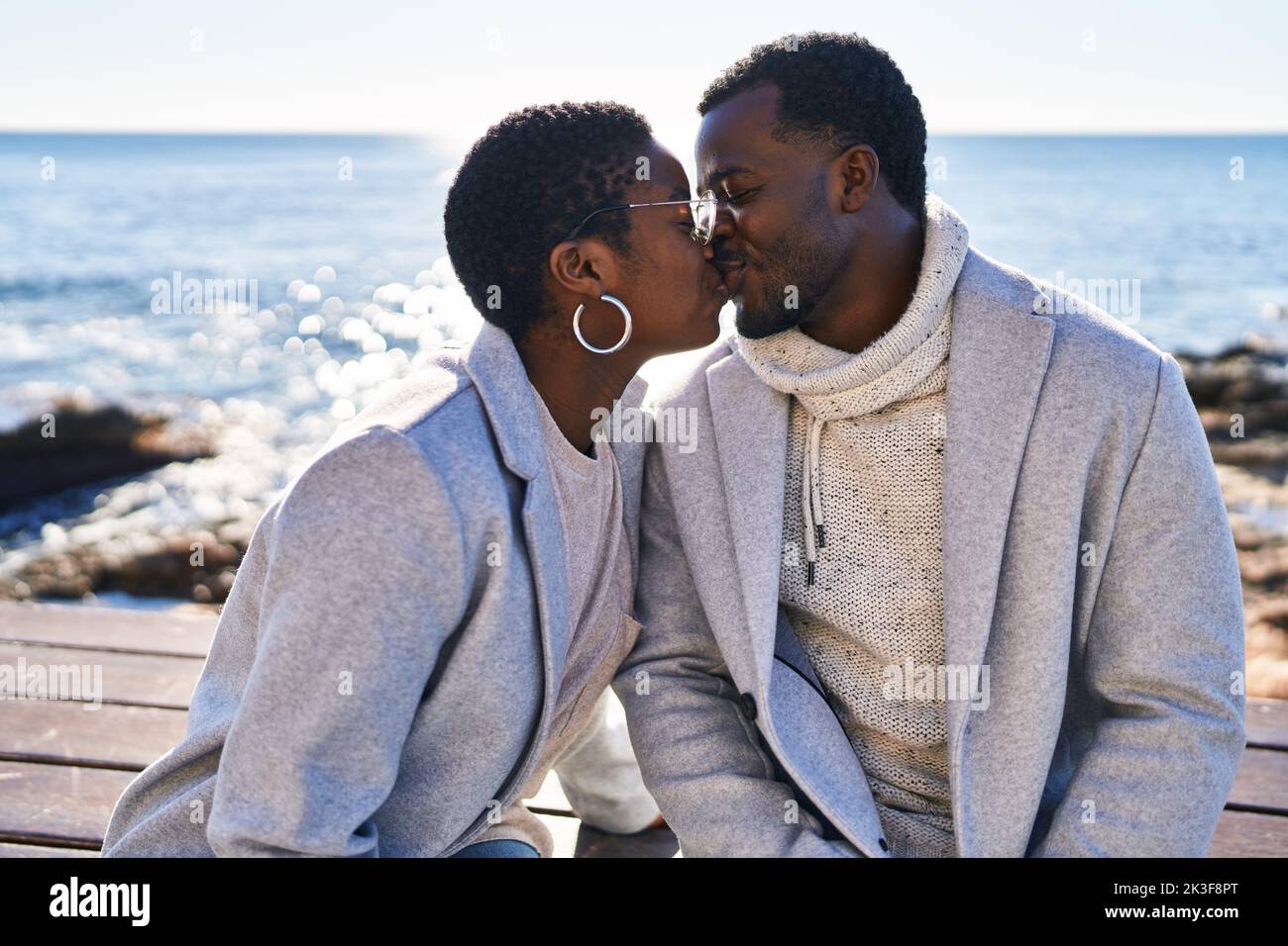 Man and woman couple sitting on bench kissing at seaside Stock Photo ...
