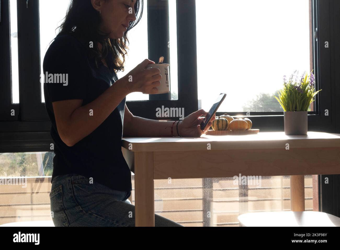 a middle-aged woman using cell phone while drinking coffee Stock Photo