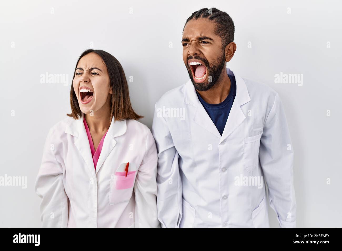Young hispanic doctors standing over white background angry and mad