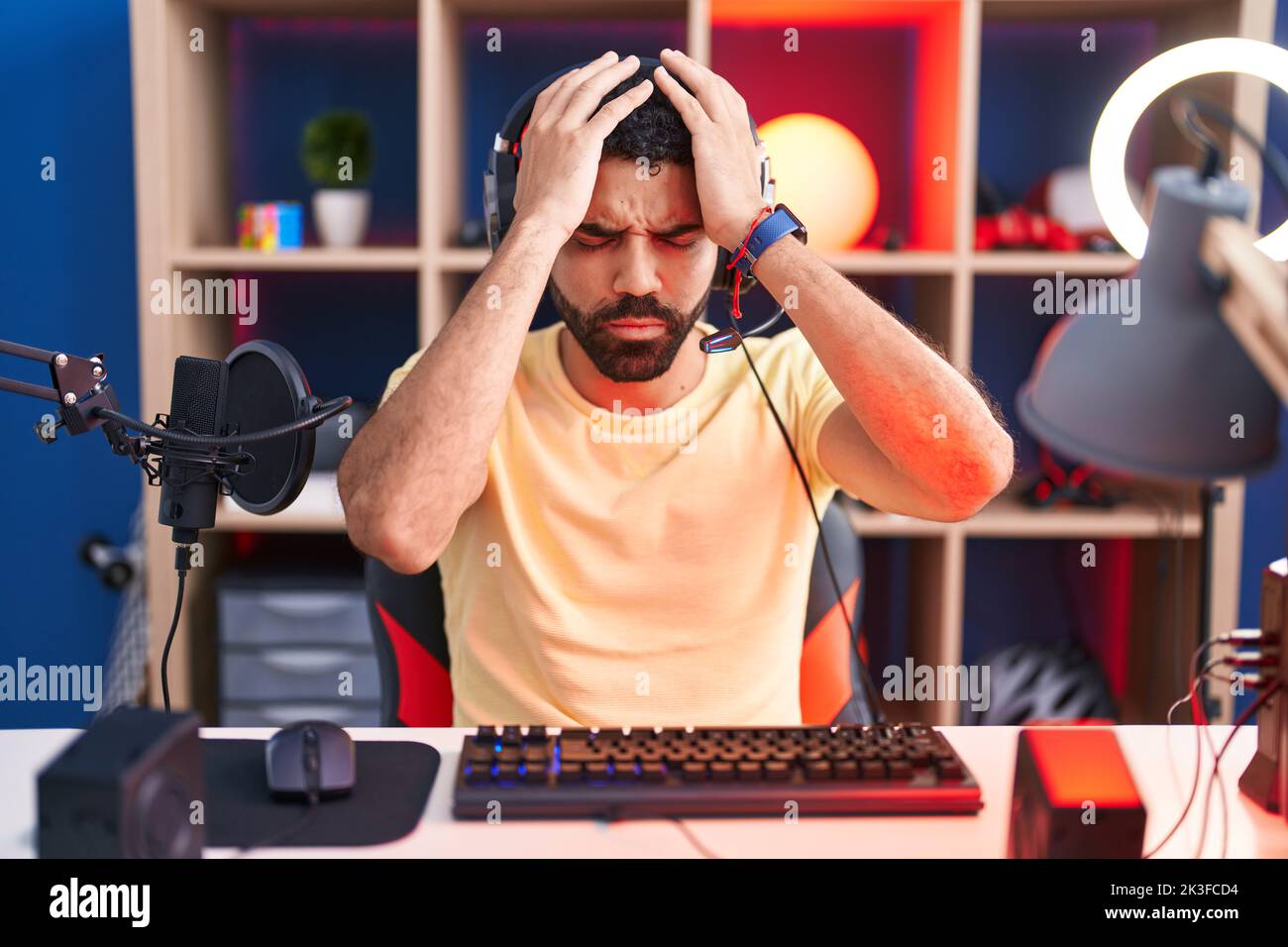 Hispanic man with beard playing video games with headphones suffering