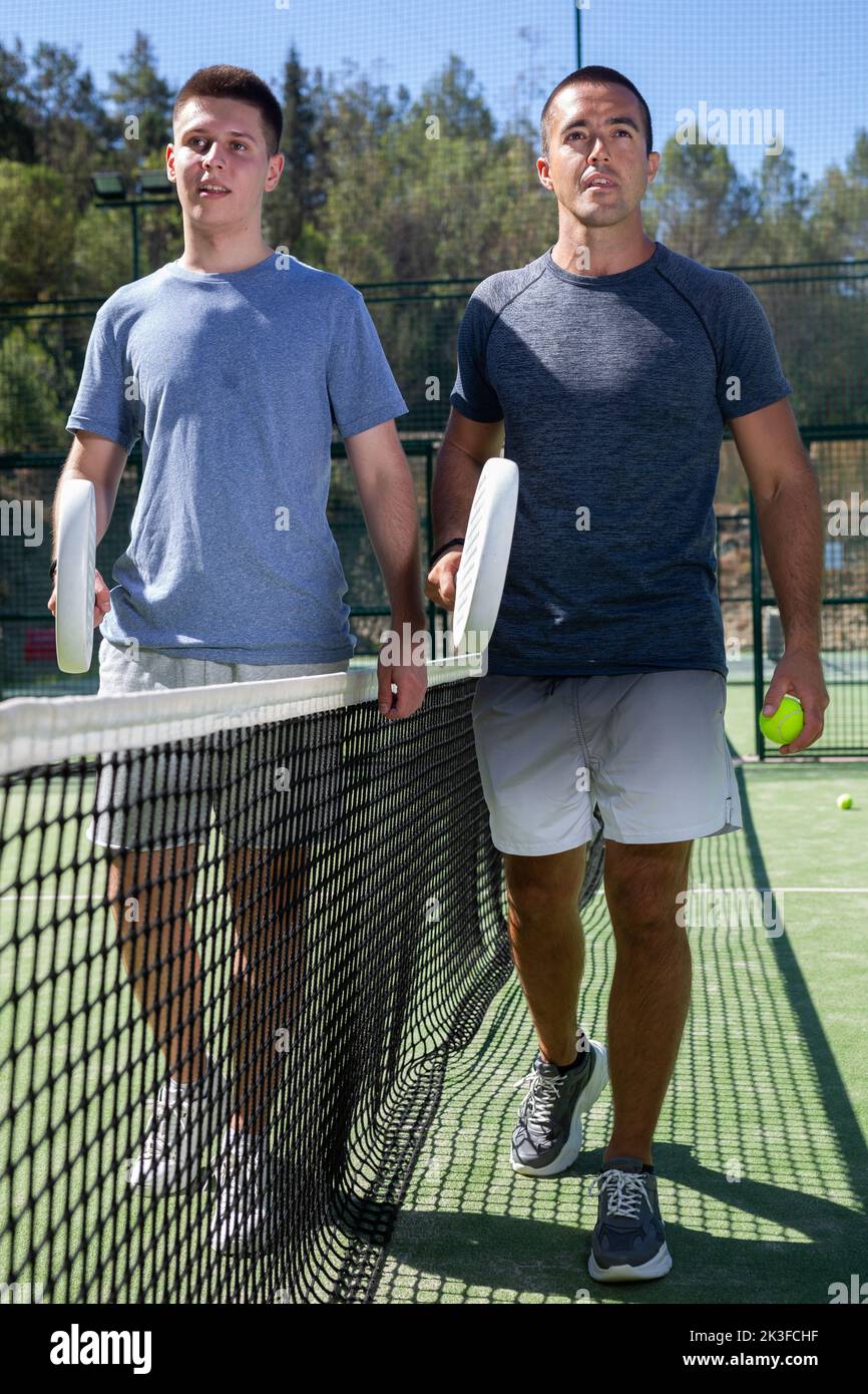 Two men with rackets in their hands chatting after playing padel on ...