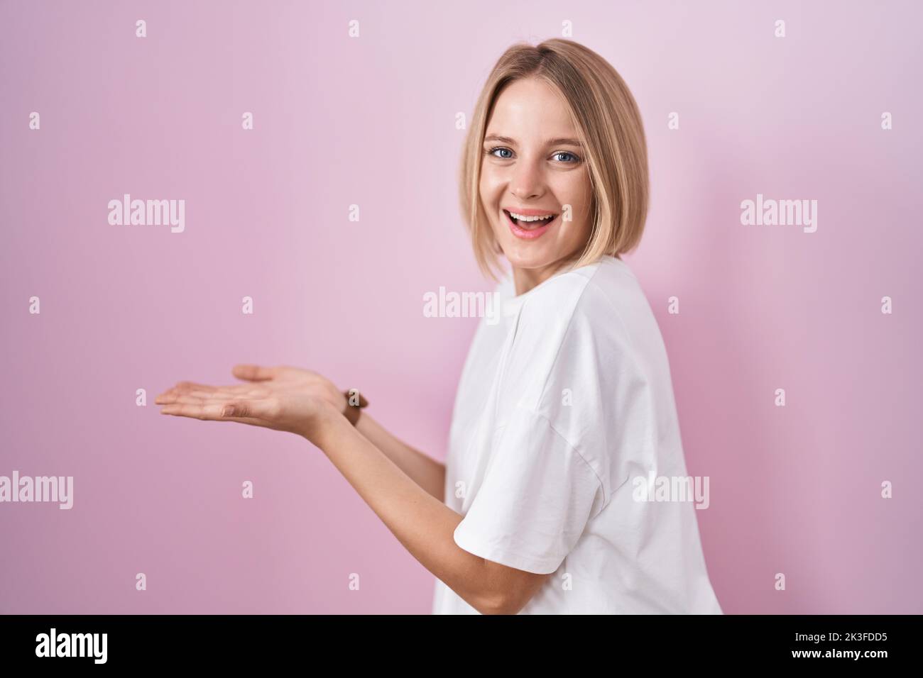 Young caucasian woman standing over pink background pointing aside with ...