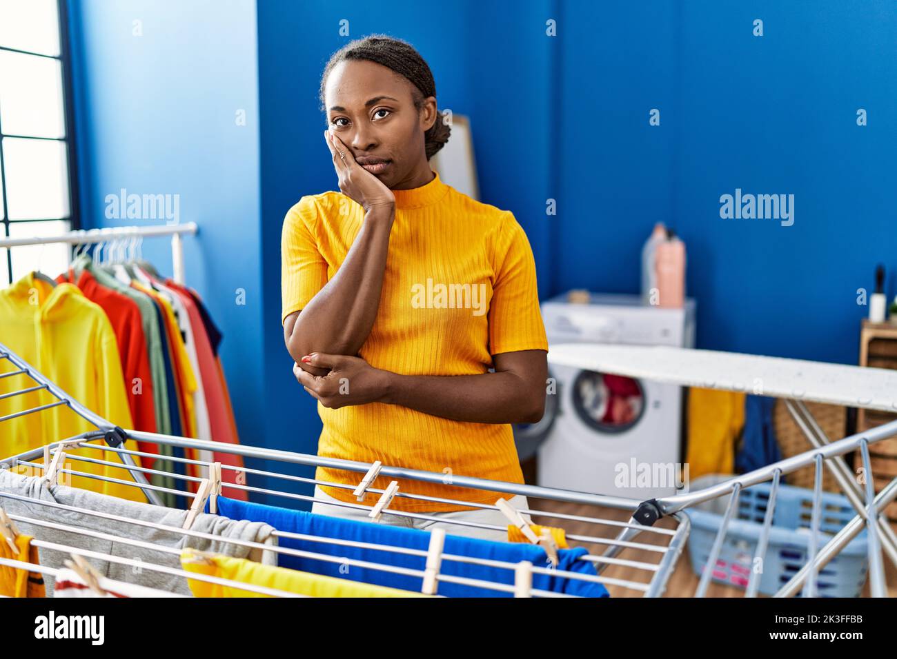 African woman hanging clothes at clothesline thinking looking tired and ...