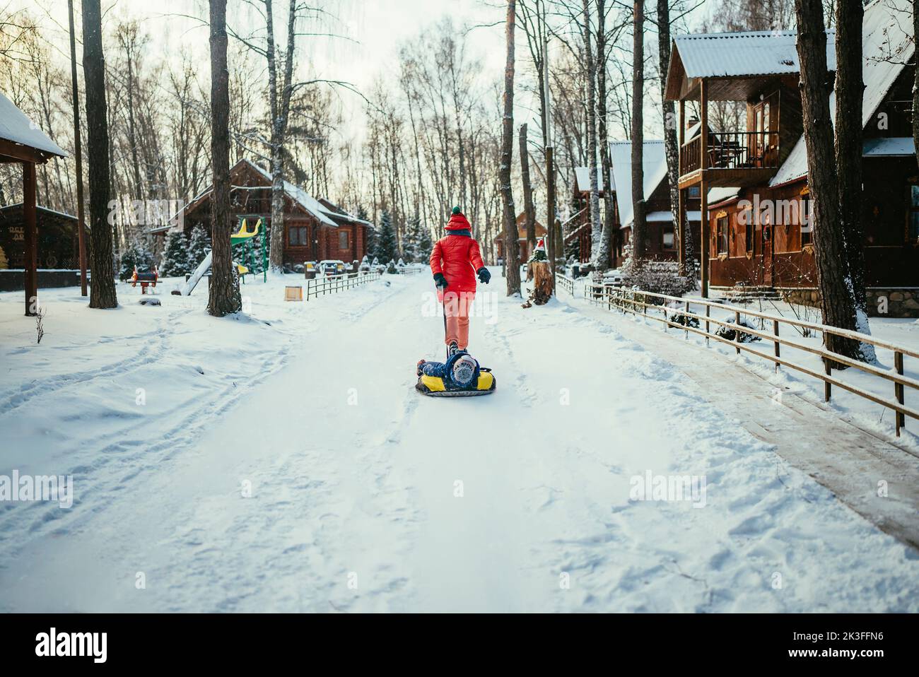 mom and little son in a blue jacket in a snowy forest ride in a tubing ...