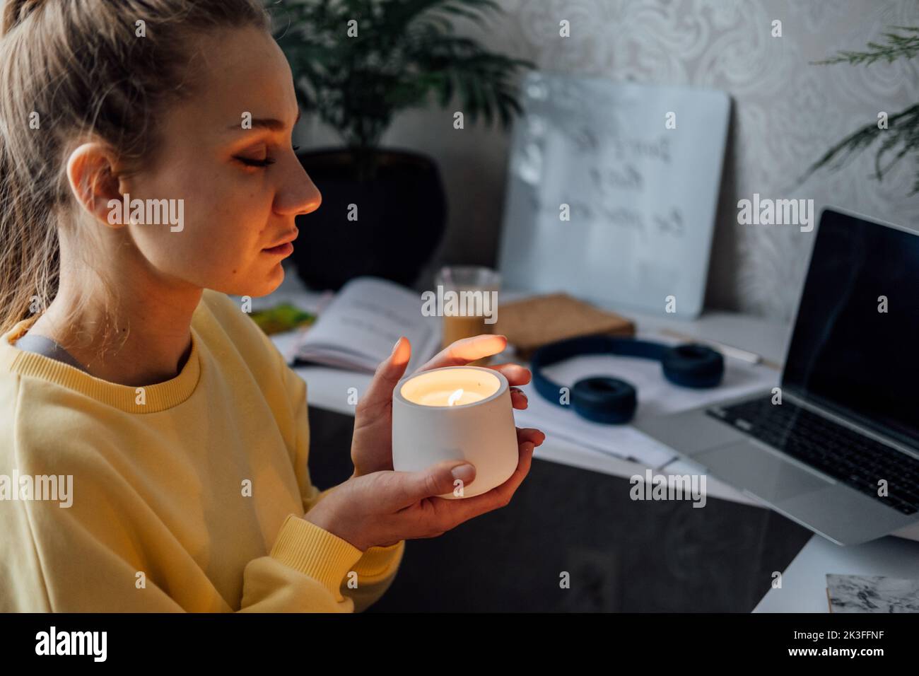 Young woman sitting on workplace at home office with lights candles, enjoy meditation, relaxing at home. Mental health, self care, No stress Stock Photo