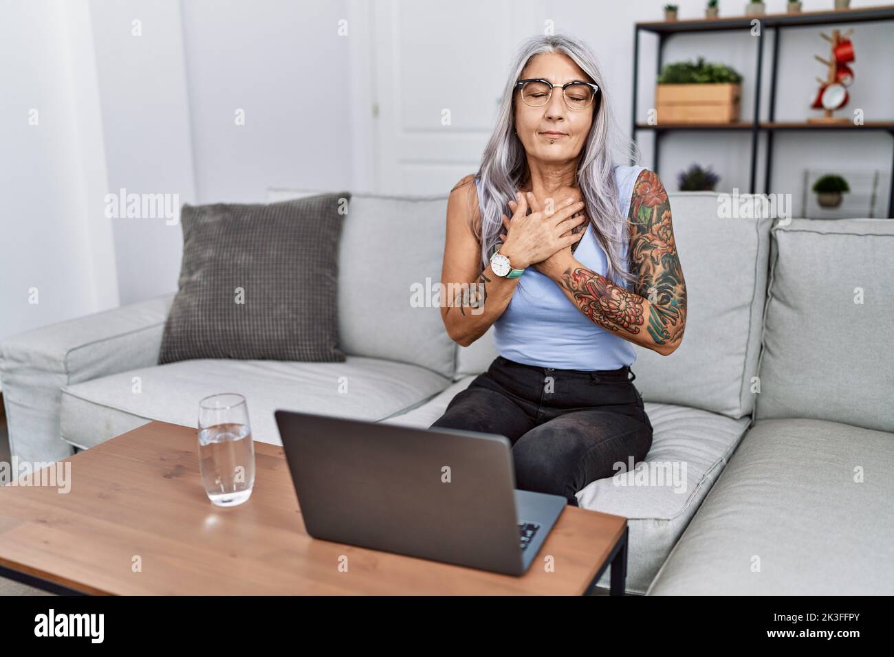 Middle age grey-haired woman using laptop at home smiling with hands on ...