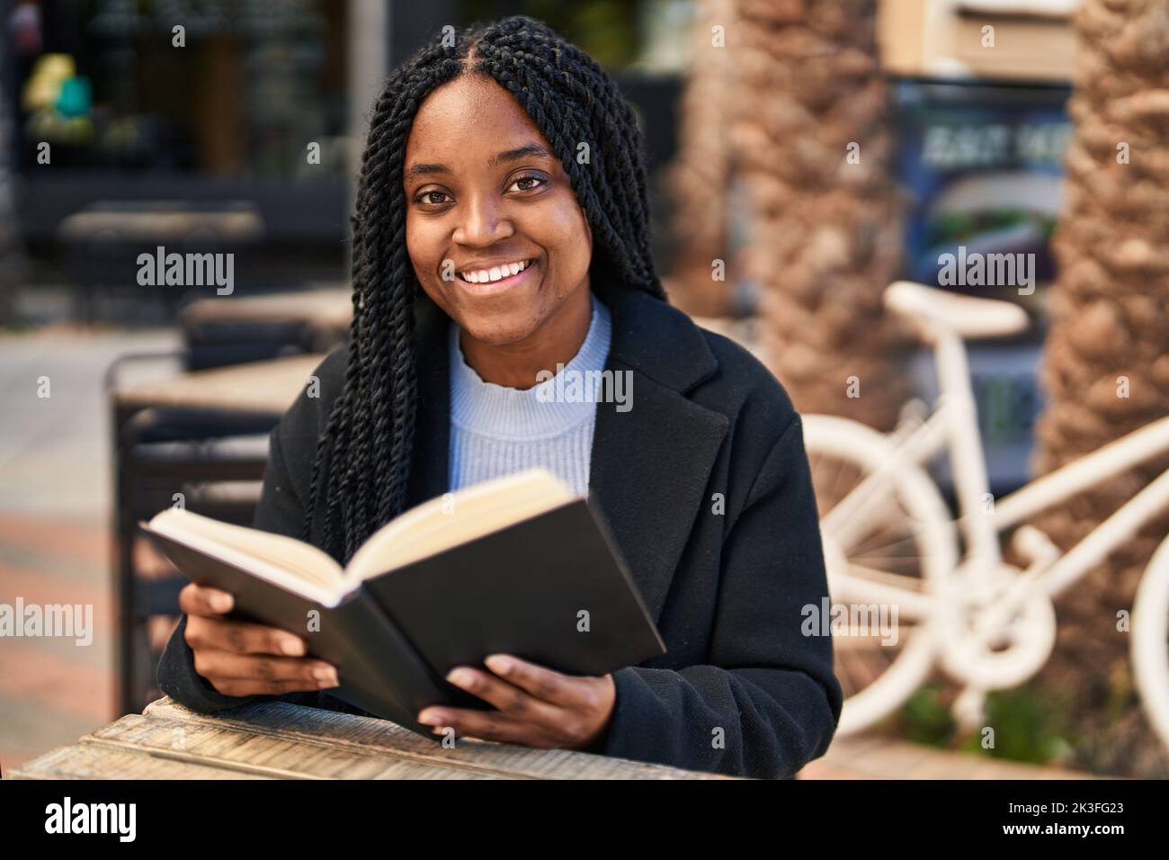 African american woman reading book sitting on table at coffee shop ...