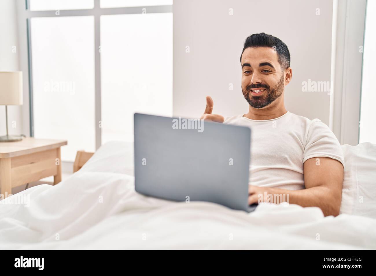 Young hispanic man with beard using computer laptop on the bed smiling ...
