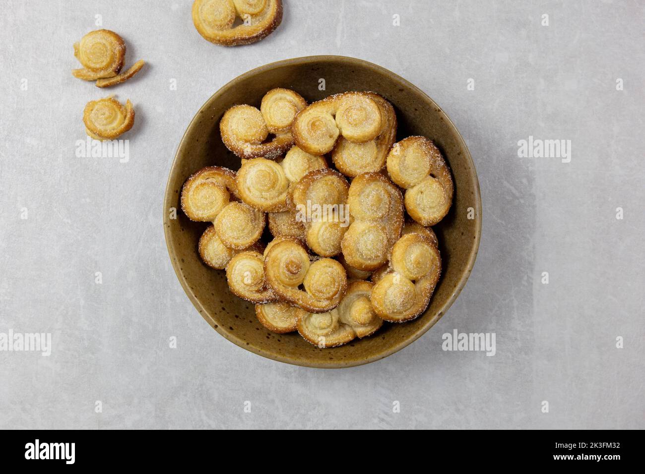 Puff pastry eyelet, Palmier cookies in a bowl with cinnamon and sugar on the light concrete background. Top view. Stock Photo