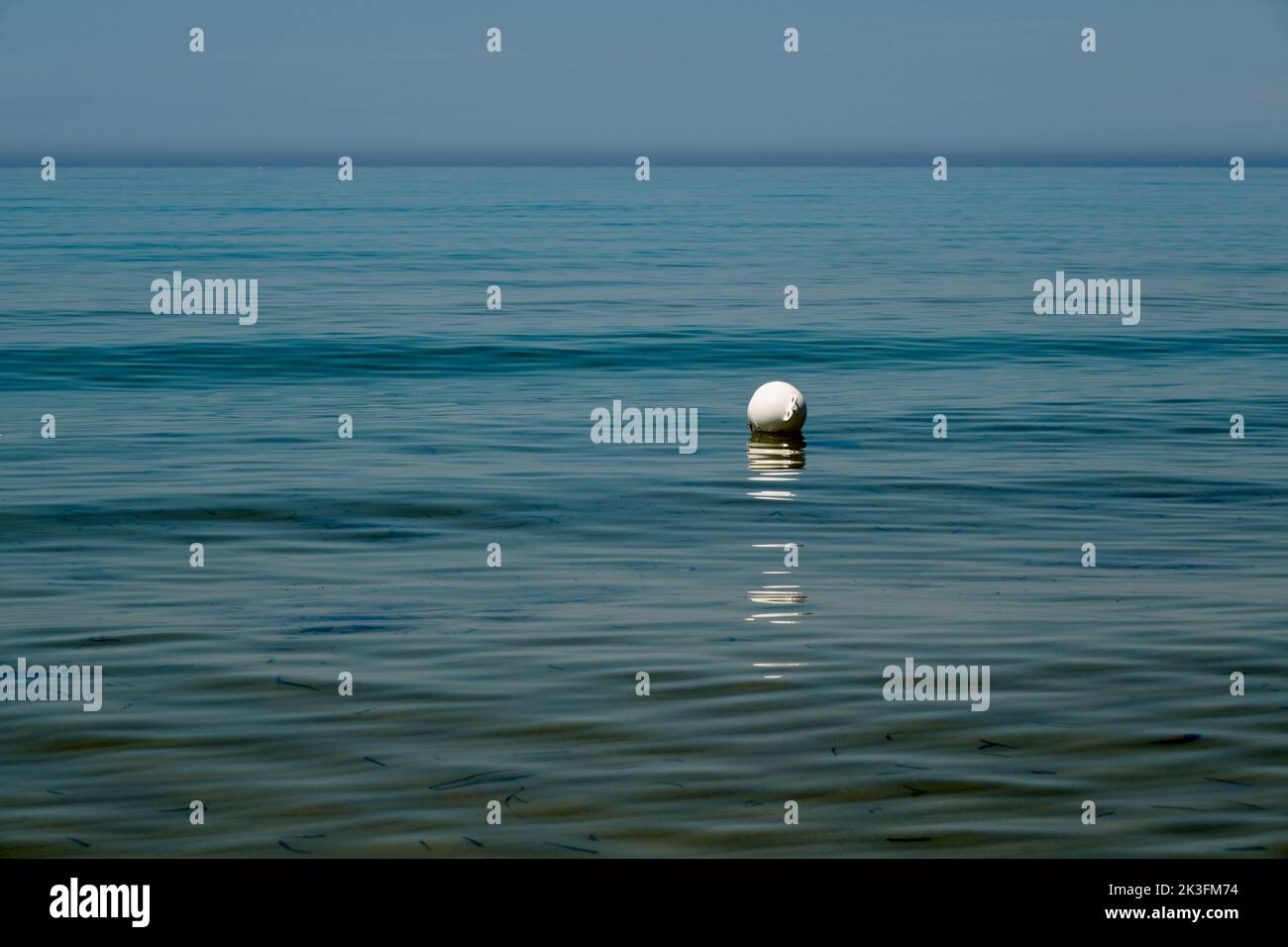 Minimalist image of a white buoy floating on the sea, seemingly isolated, with the horizon line dividing sky and sea in the background. Sicily summer. Stock Photo