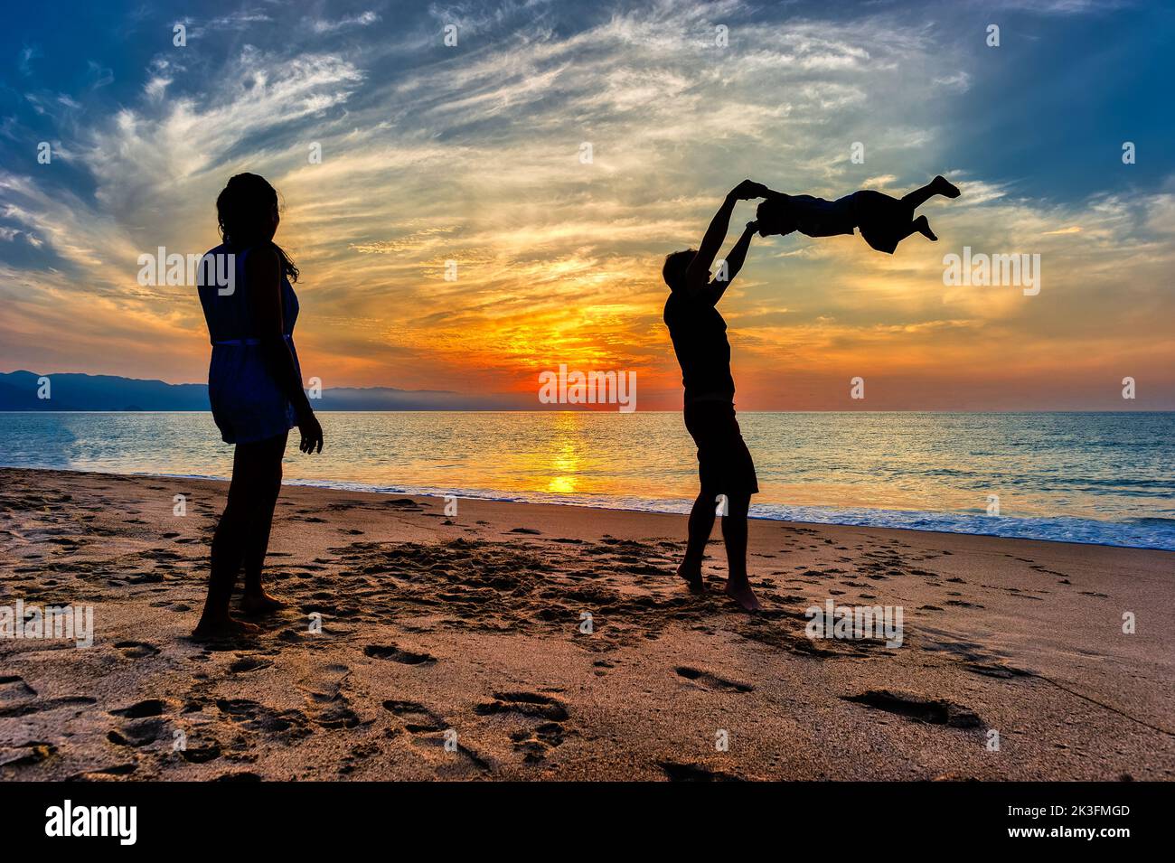 A Father is Playing With His Son On the beach As A Mother Watches On Stock Photo