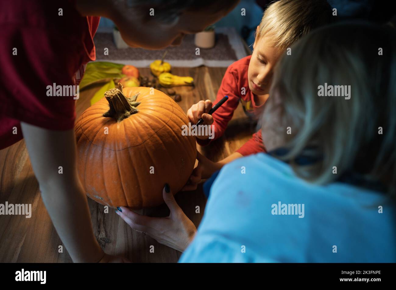 Three children, siblings, drawing on a pumpkin they will carve for halloween holiday season. Stock Photo