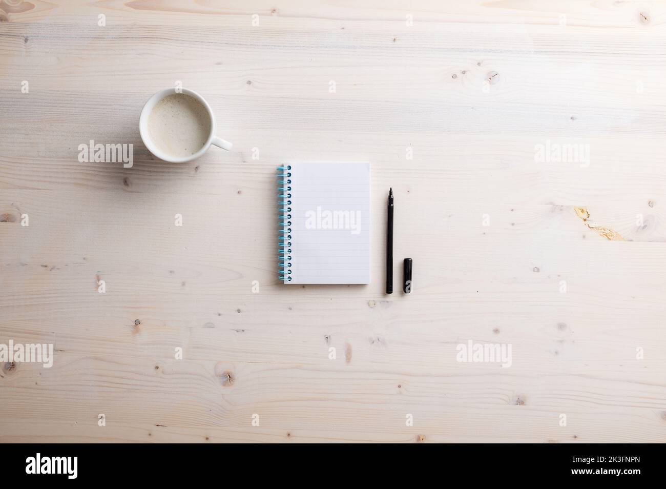 Blank spiral notebook and open black spiral pen placed on simple wooden desk with a cup of fresh coffee. Stock Photo