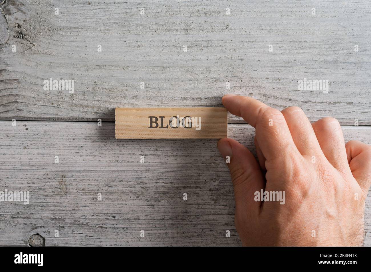 Male hand placing a wooden peg with Blog sign on it over textured white wooden backround. Stock Photo