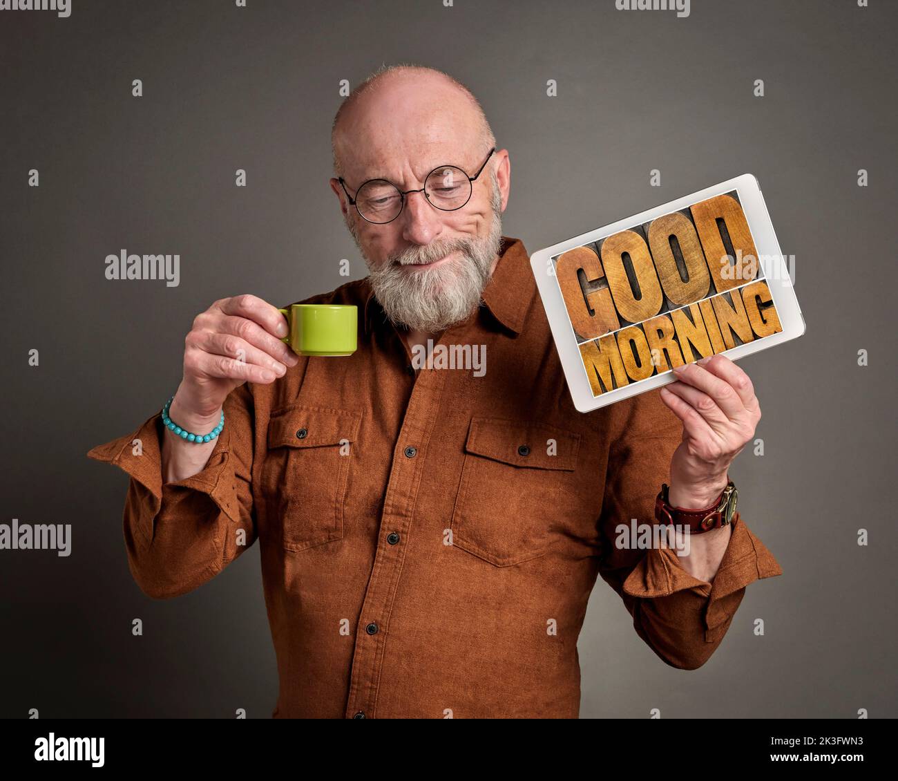 Good Morning - smiling senior man is drinking coffee and showing a digital tablet with text in wood type, positive start of  a new day concept Stock Photo
