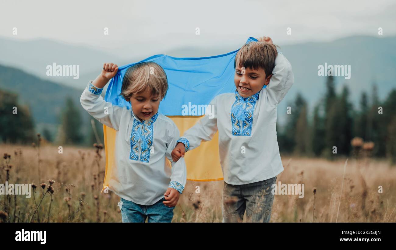 Happy glad boys - Ukrainian patriots children jumping, rejoyces with national flag on meadow of Carpathian mountain. Ukraine, family, brothers twins Stock Photo