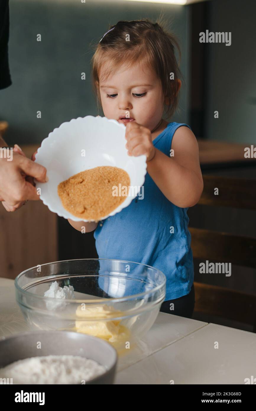 The mother helping her daughter turn the bowl of cocoa over the dough prepared for baking. For lifestyle design. People lifestyle. Stock Photo