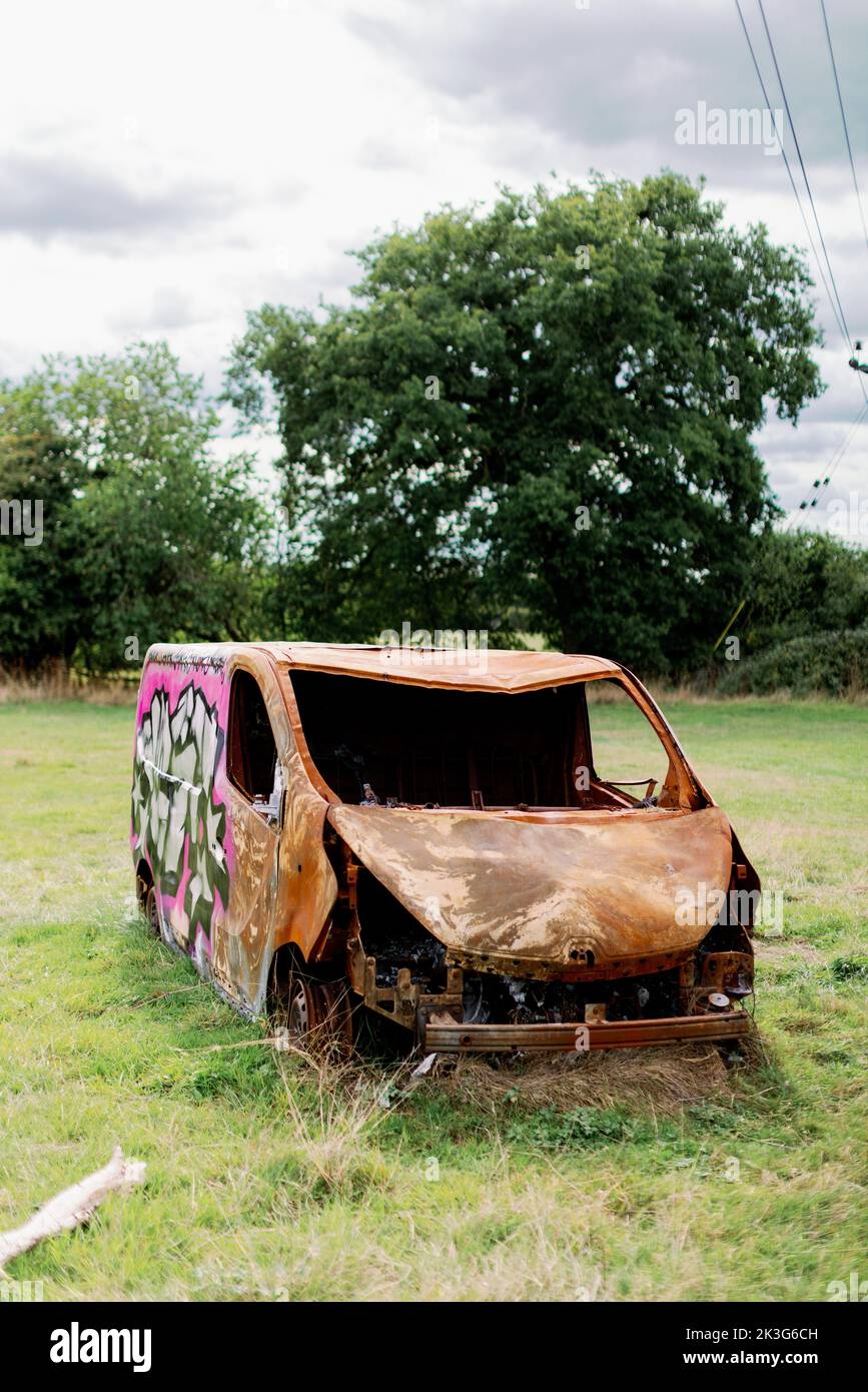 A burnt out worker's van rusty and abandoned in the middle of a field in the countryside Stock Photo