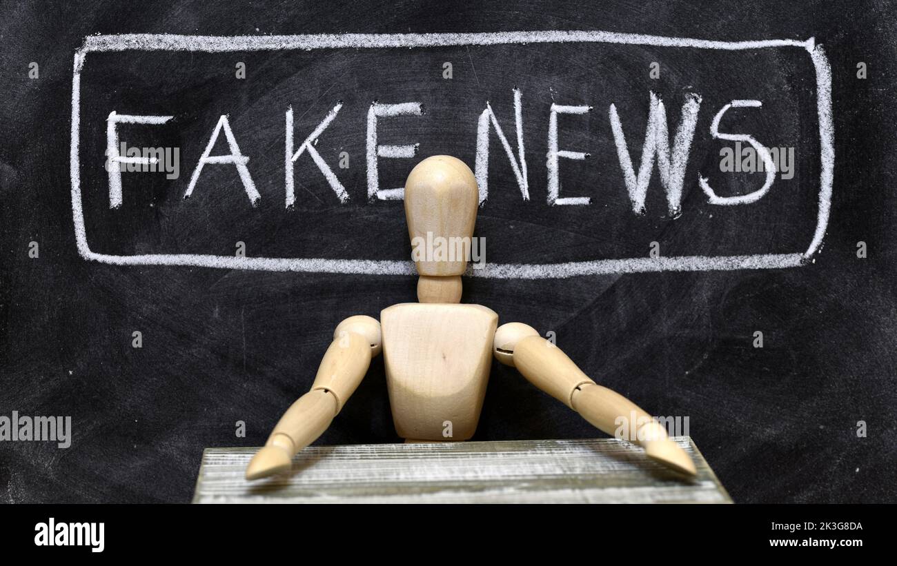 Muñeco articulado de madera sentado a modo de presentador de noticias falsas, fake news Stock Photo