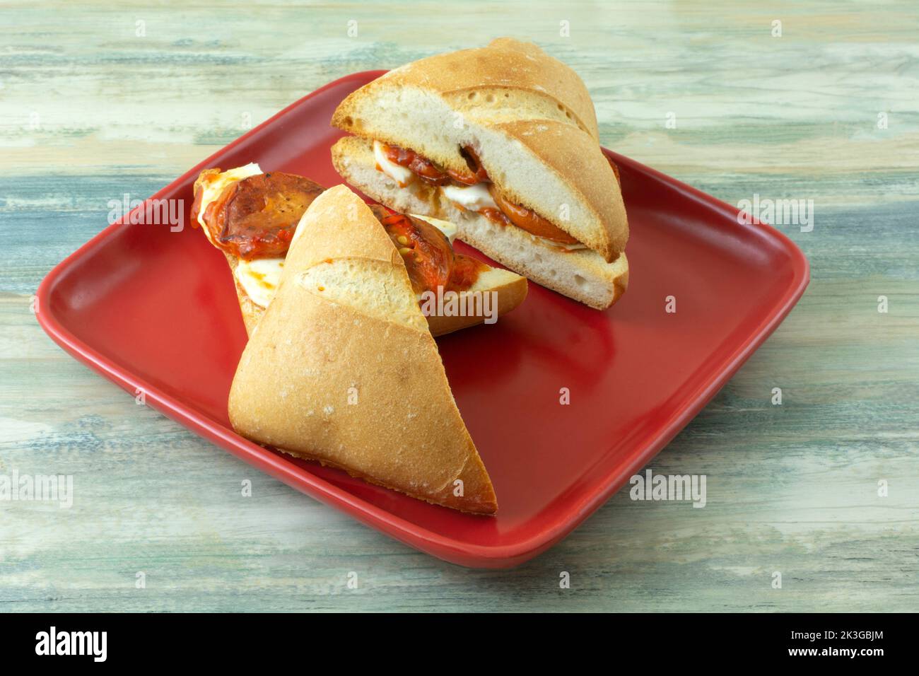 Fresh mozzarella cheese and roasted tomato sandwich with red pepper spread on roll on red plate Stock Photo