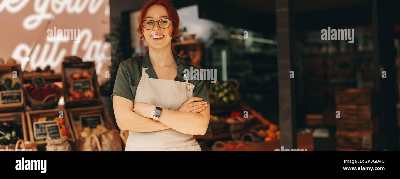 Successful supermarket owner smiling at the camera while standing in the fresh produce section of her grocery store. Happy young woman running a small Stock Photo