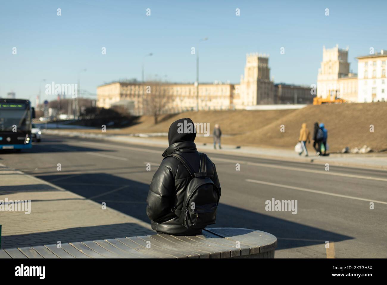 Guy is waiting for bus. Man in black clothes. Man is waiting for transport in city. Sitting on bench. Stock Photo