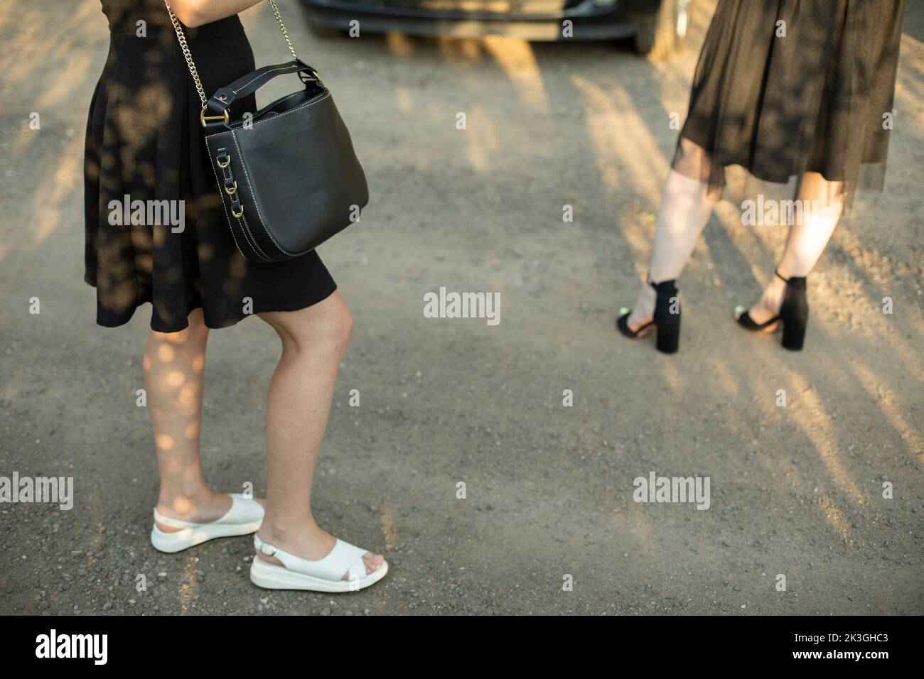 Girl with black bag in black dress on street. Girls in parking lot. Clothing details. Young girls in summer in city. Stock Photo