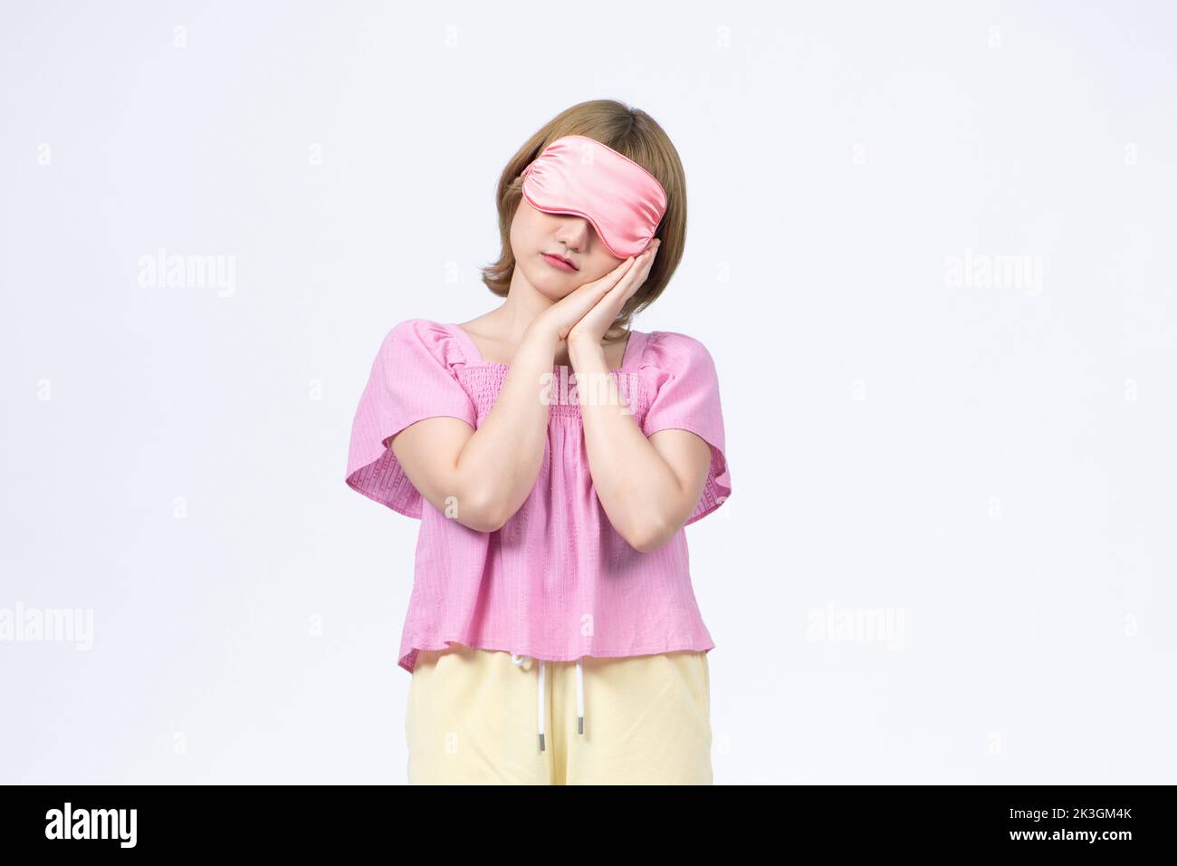 Portrait of young woman in nightwear with sleep mask on white background Stock Photo