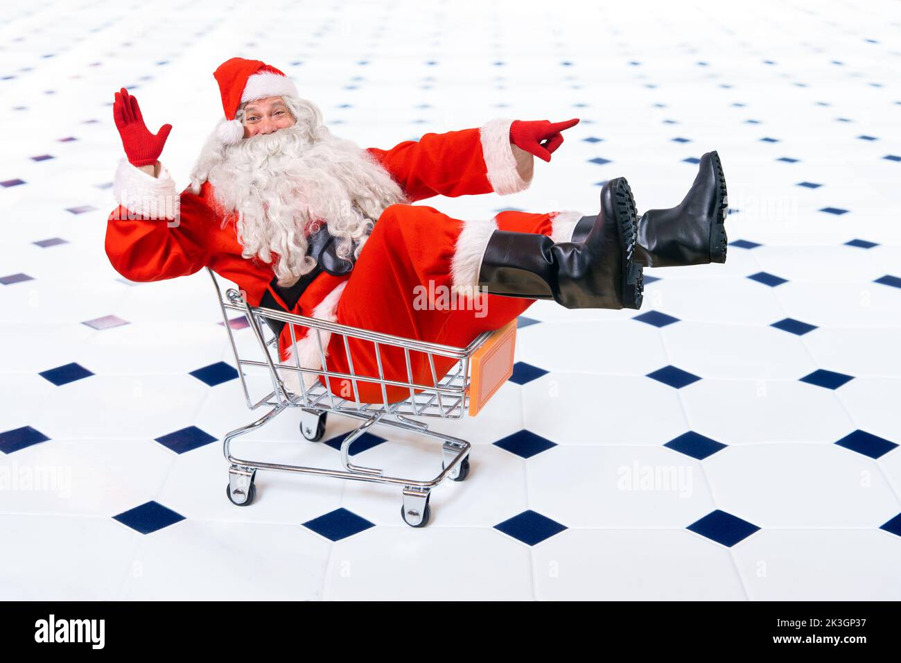 Cheerful Santa Claus sits in a shopping cart and points the direction with his hand Stock Photo