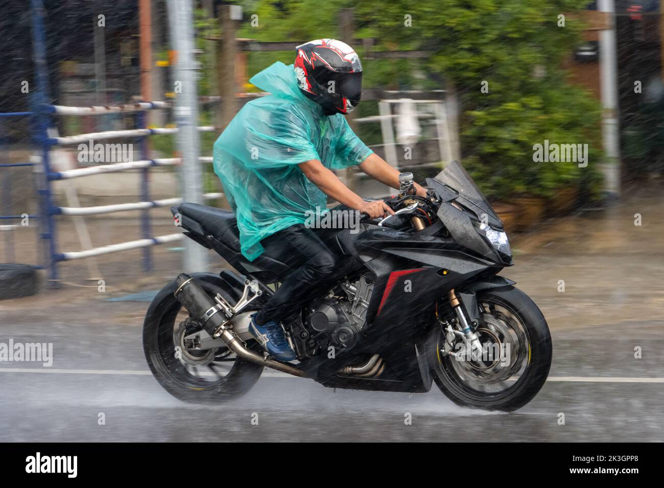 A man in a raincoat rides a motorcycle on the street in heavy rain Stock Photo